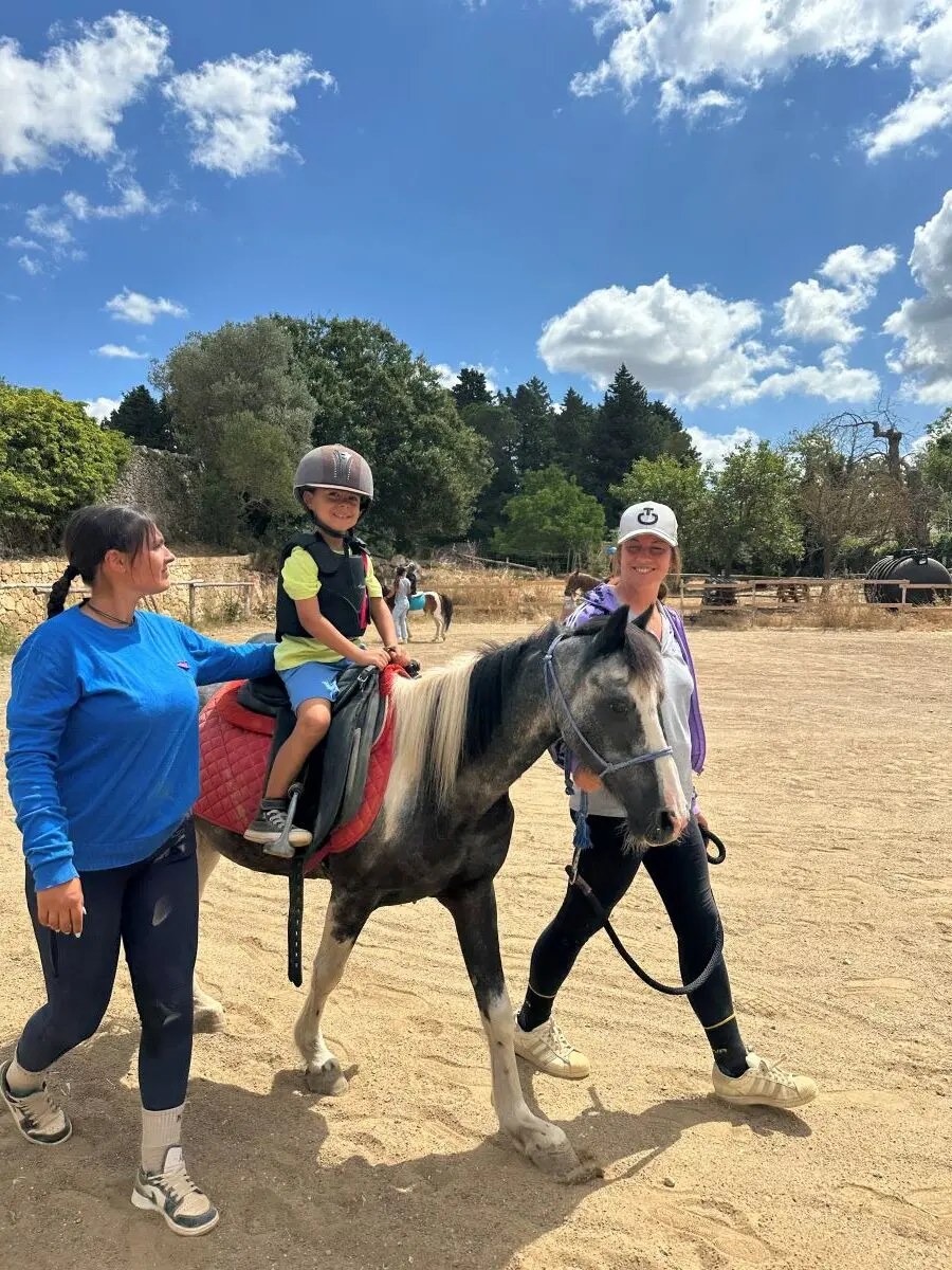 A child on a pony led by two instructors in an outdoor riding arena