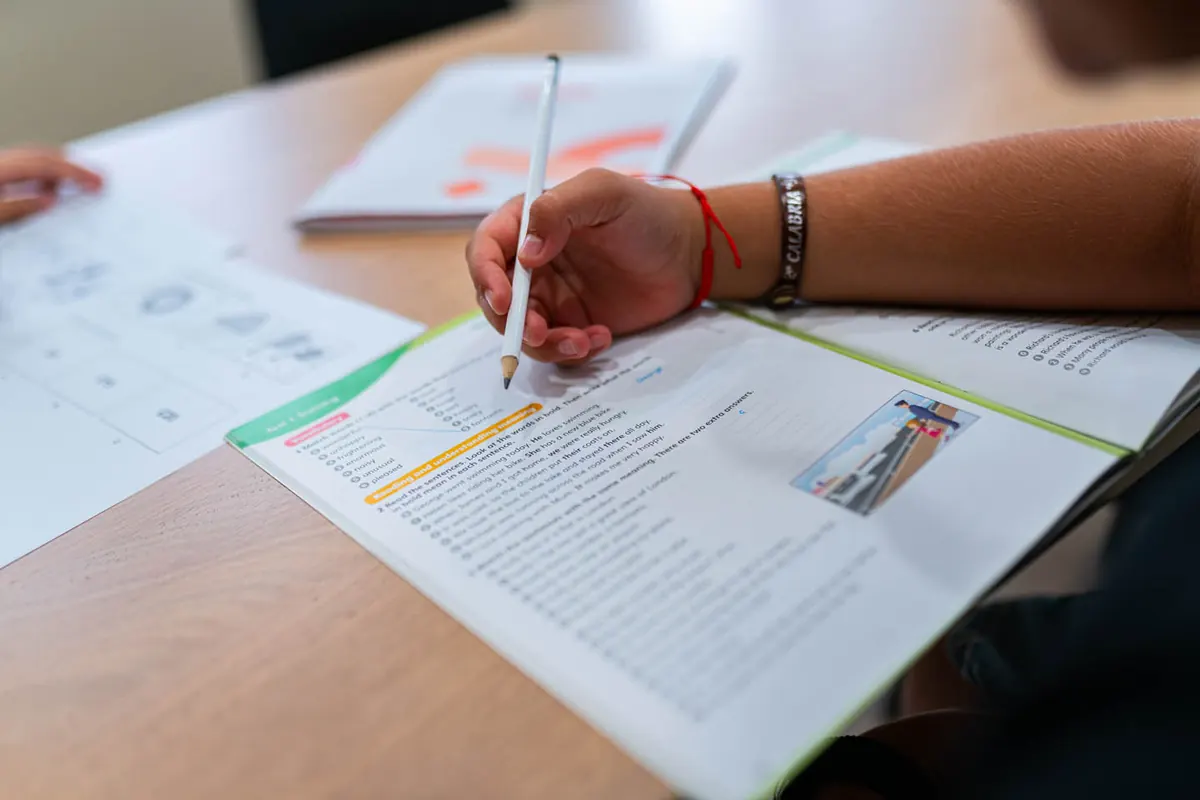 Mano di uno studente scrive in un quaderno di inglese su un banco di legno, con la matita