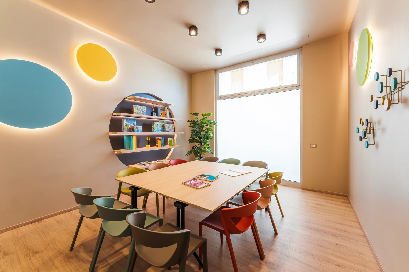 A KOKOland Monopoli classroom with colourful lit circles, a round bookcase and chairs in many colours