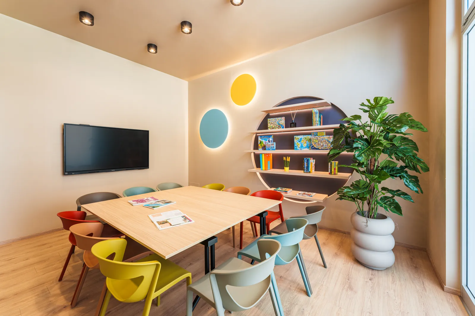 Classroom at the KOKOland school in Monopoli with a large table, colourful chairs, a round bookshelf and the interactive whiteboard
