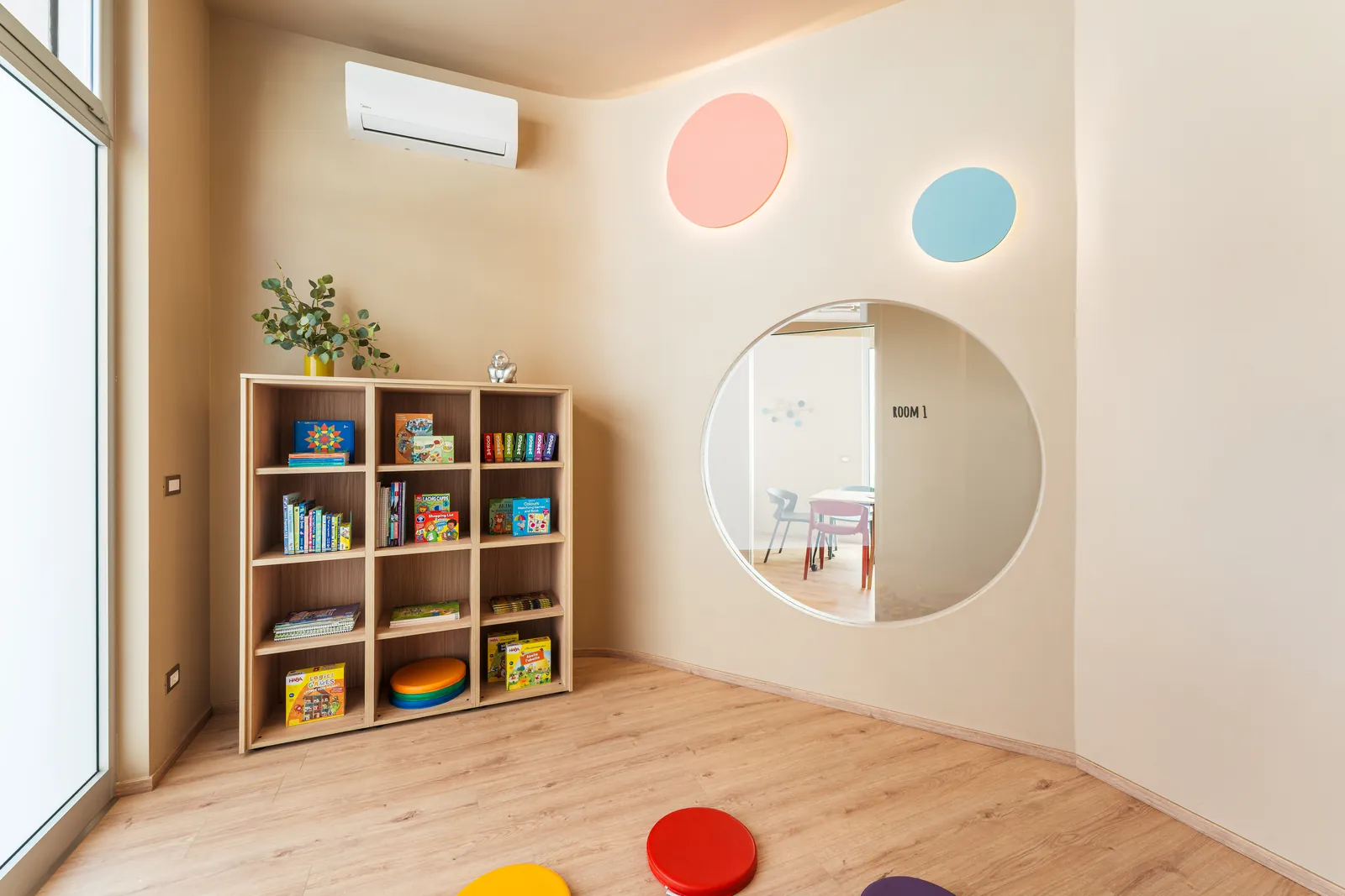 A wooden bookcase full of games next to a large porthole window