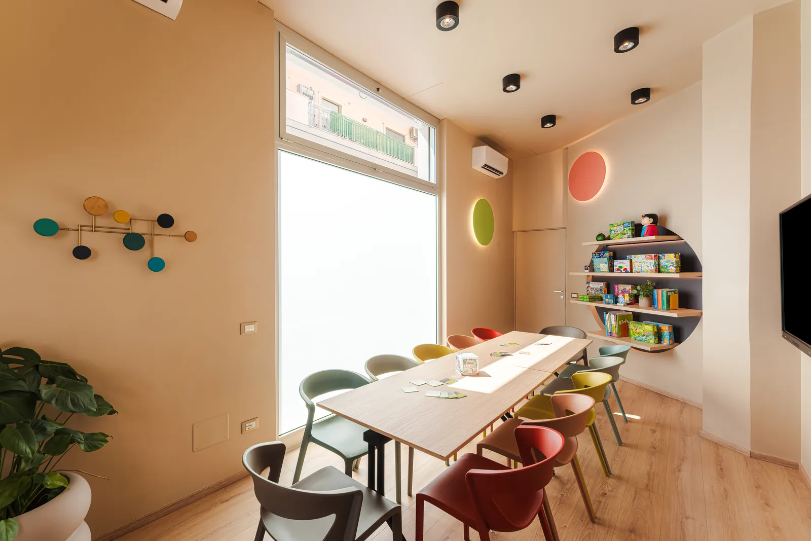 A bright classroom with a long table, colourful chairs and the round bookcase
