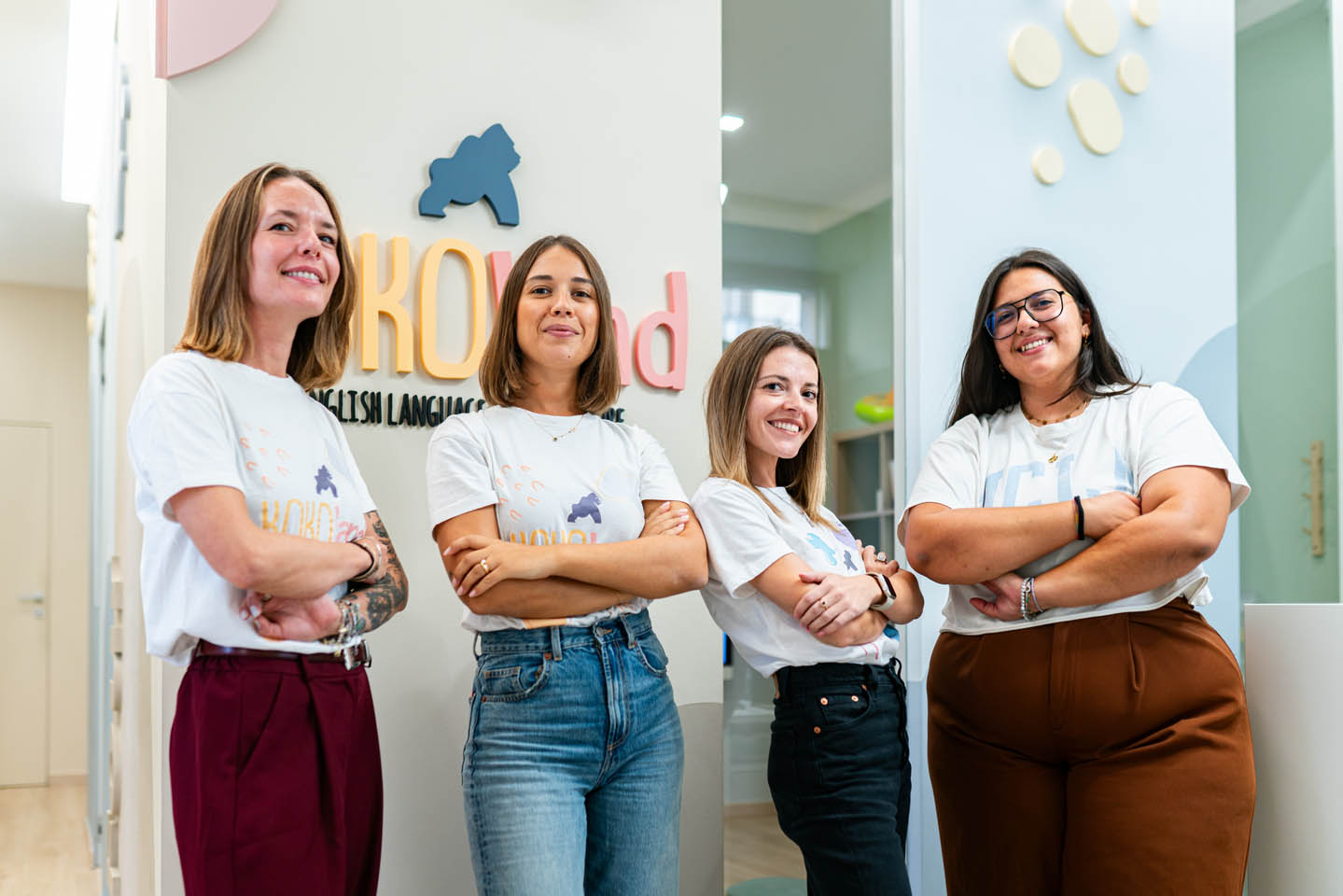 Four KOKOland teachers smiling with folded arms in front of the school logo